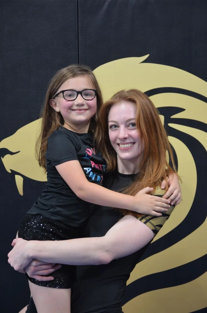 Mooresville Brazilian Jiu-Jitsu instructor Brooke with a young female student in front of the academy's tiger logo