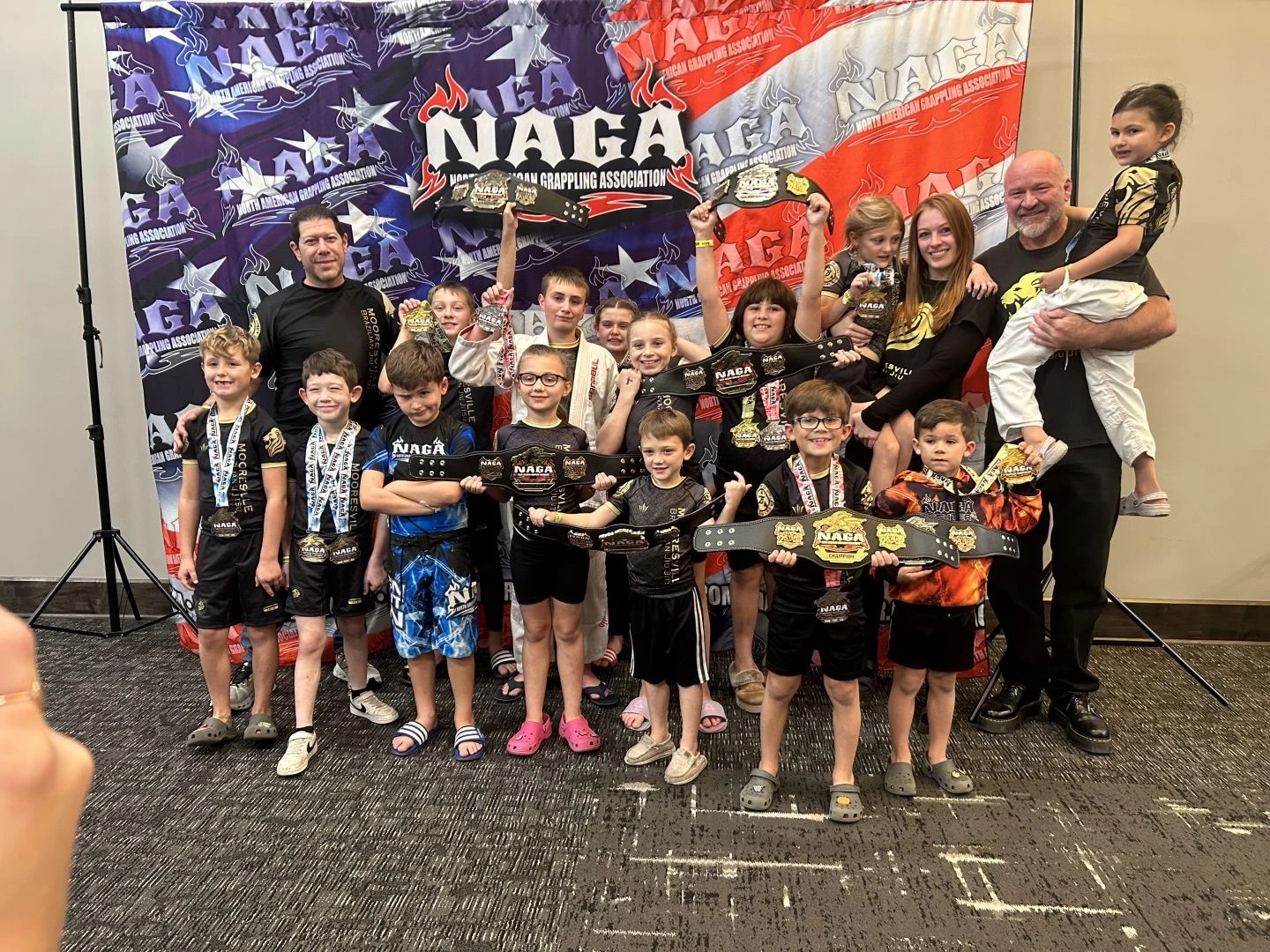 Mooresville Brazilian Jiu-Jitsu competition team posing with championship belts at NAGA tournament