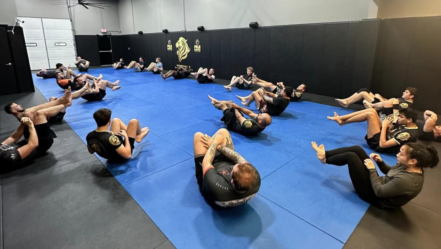 Full Mooresville Brazilian Jiu-Jitsu class on the mat — students in conditioning circuit, wide view of the training floor